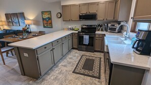 A modern kitchen with a central island, stainless steel appliances, and a dining area with a sofa and table. - Peaceful Fraser Condo Retreat, Close to Winter Park! (Fraser)