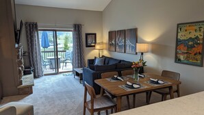 A modern living room with a sofa, a dining table, and a coffee table. There is a sliding glass door leading to an outdoor area with a patio table and chairs. - Peaceful Fraser Condo Retreat, Close to Winter Park! (Fraser)