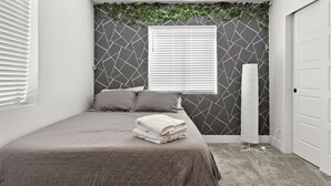 A bedroom with a bed, a window with blinds, a wall-mounted radiator, and a door. - Spacious 5 Bedroom Home with large kitchen in the Heart of Central Phoenix ☀️ (Phoenix)