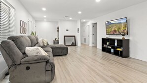 A modern living room with a grey sectional sofa, a flat-screen TV mounted on the wall, and a black entertainment unit. - Spacious 5 Bedroom Home with large kitchen in the Heart of Central Phoenix ☀️ (Phoenix)