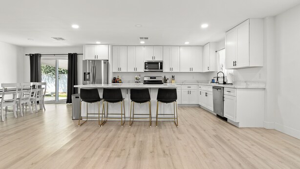 A modern kitchen with white cabinets, a central island with bar stools, and a dining area with a table and chairs. - Spacious 5 Bedroom Home with large kitchen in the Heart of Central Phoenix ☀️ (Phoenix)