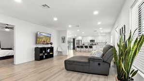 A modern living room with a sectional sofa, a flat-screen TV, a bookshelf, and a potted plant. - Spacious 5 Bedroom Home with large kitchen in the Heart of Central Phoenix ☀️ (Phoenix)