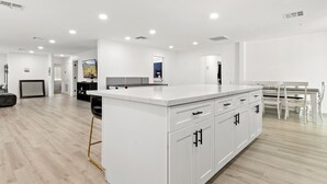A modern kitchen with white cabinetry, a central island, and a dining area with a white table and chairs. - Spacious 5 Bedroom Home with large kitchen in the Heart of Central Phoenix ☀️ (Phoenix)