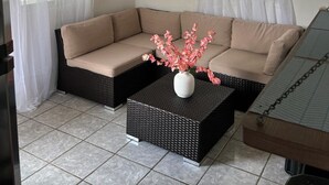 A cozy living room with a beige sectional sofa, a black wicker coffee table with a white vase, and two windows with patterned curtains. - Villa ático beach house,pool,wifi,Netflix,backyard (Salinas)