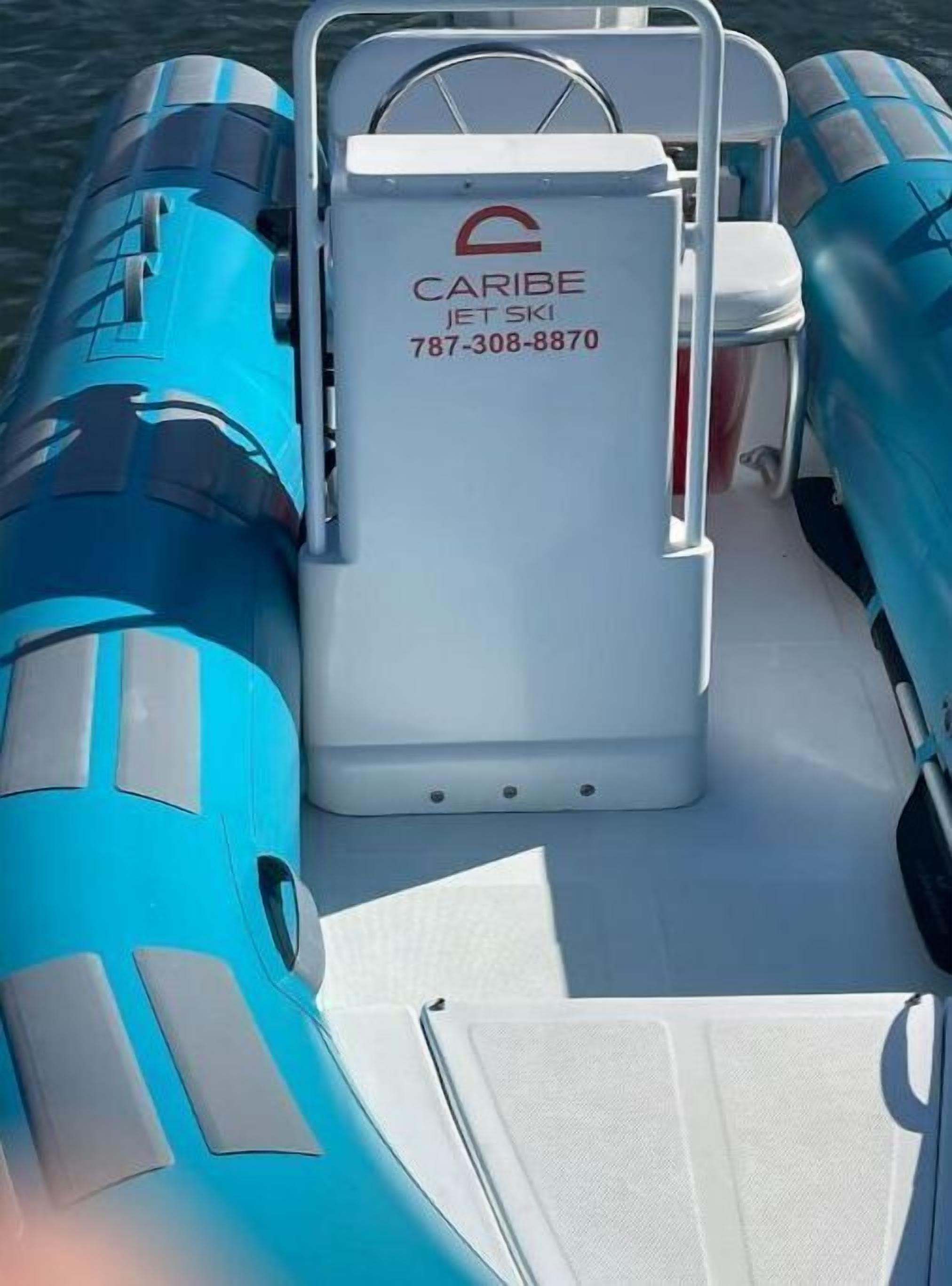 A boat with a white cabin and blue exterior, featuring a contact number and logo for CARIBE IFT SKI.