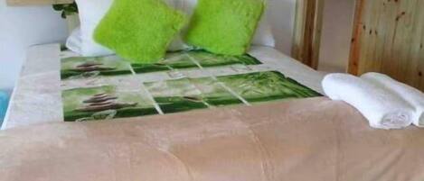 Una cama con una colcha verde y blanca estampada, dos almohadas verdes y una toalla blanca.