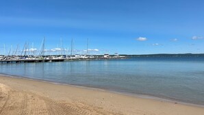 Un port de plaisance avec des bateaux amarrés, une plage de sable et un ciel bleu dégagé.