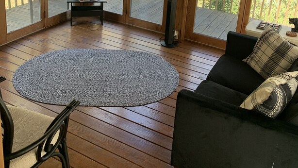 Une terrasse en bois avec un canapé noir et un tapis rond, donnant sur une pelouse verdoyante où flotte un drapeau américain.