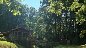 Une cabane en bois dotée d’une terrasse, entourée d’une végétation luxuriante et bordée d’un petit ruisseau.