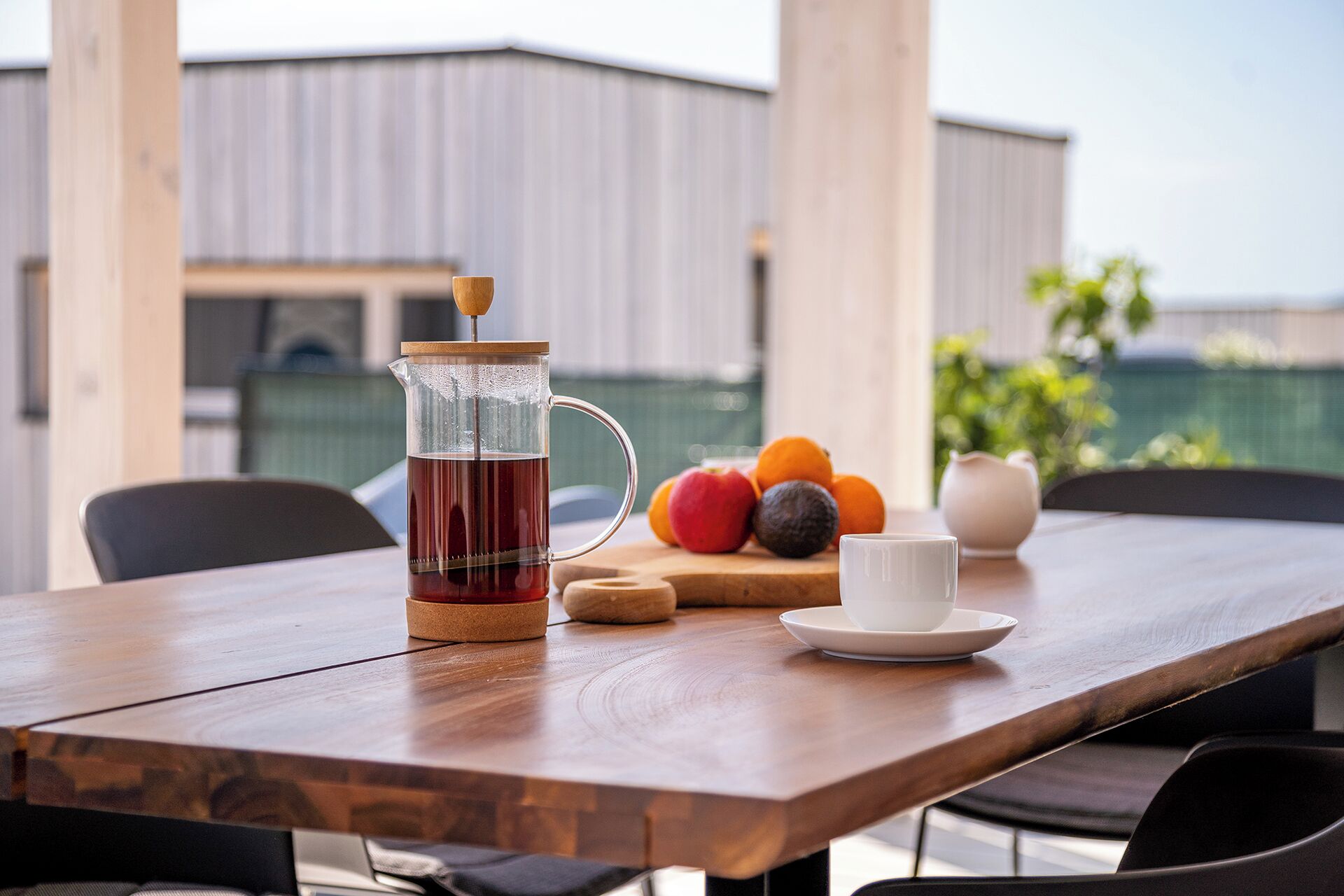 A wooden table with a coffee press, a cup, and a plate with fruits.