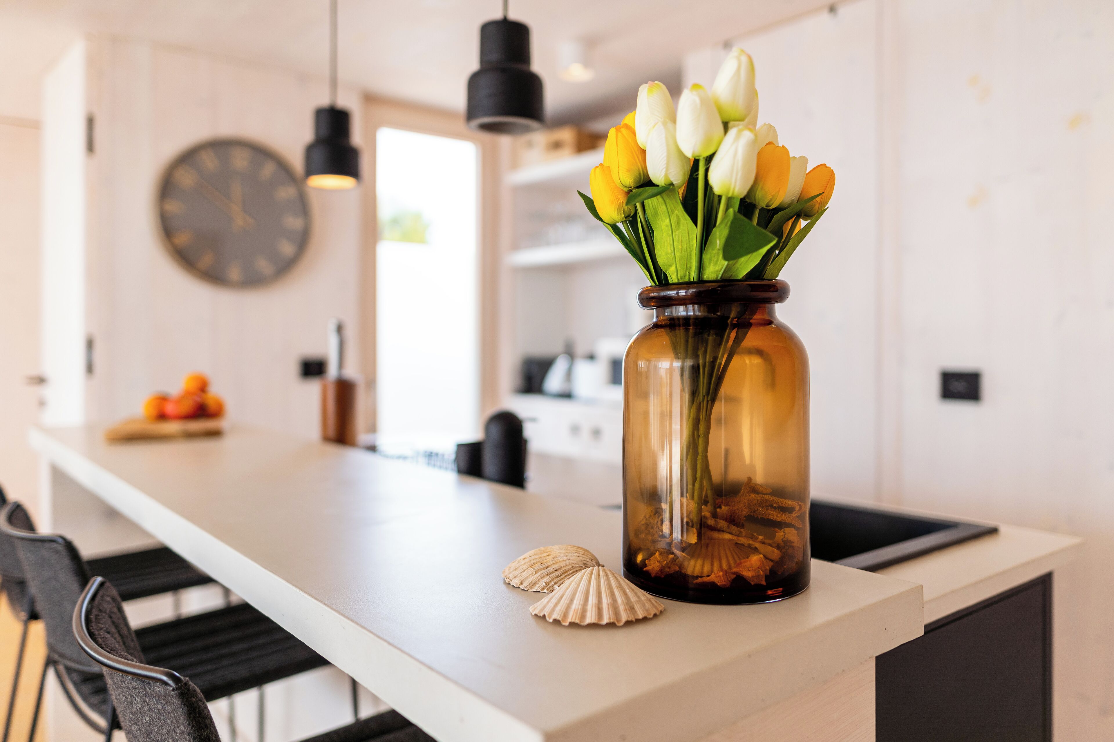 Eine Küchenarbeitsplatte mit einer Tulpenvase, einer Muschel und einer Wanduhr.