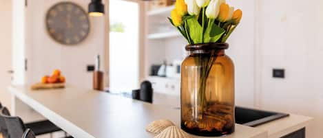 A kitchen counter with a vase of tulips, a seashell, and a clock on the wall.