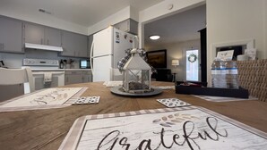 A modern kitchen with white cabinets, a stove, and a refrigerator. There is a dining table with placemats and a candle centerpiece.
