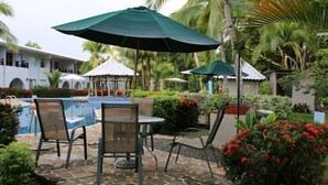 Un espace piscine agrémenté de chaises longues et de parasols, entouré de palmiers et de fleurs rouges.
