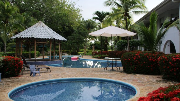 Une piscine agrémentée d’un kiosque, de chaises longues et d’une table avec un parasol.