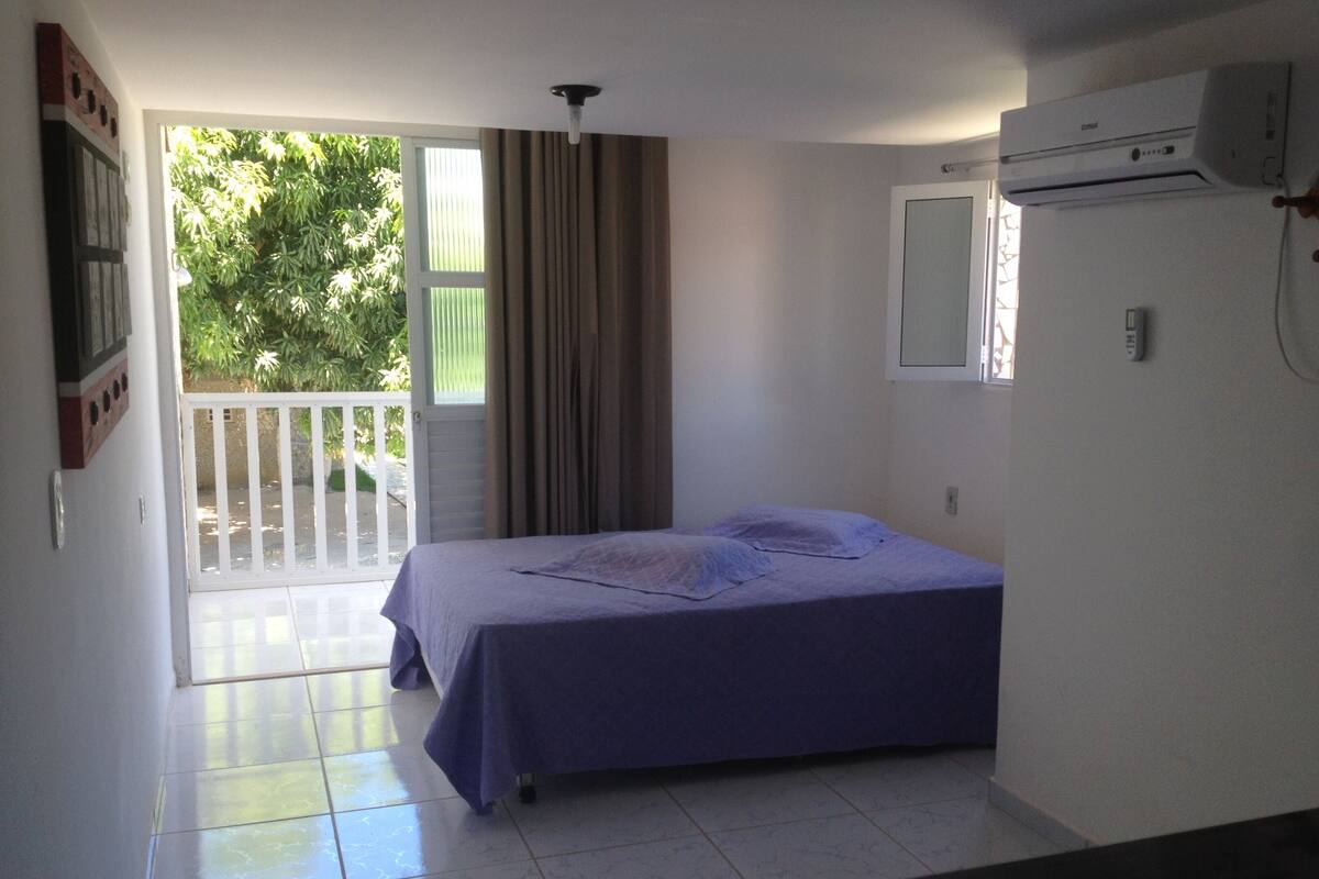Une chambre avec un lit, une fenêtre, un climatiseur et une vue sur la verdure environnante.
