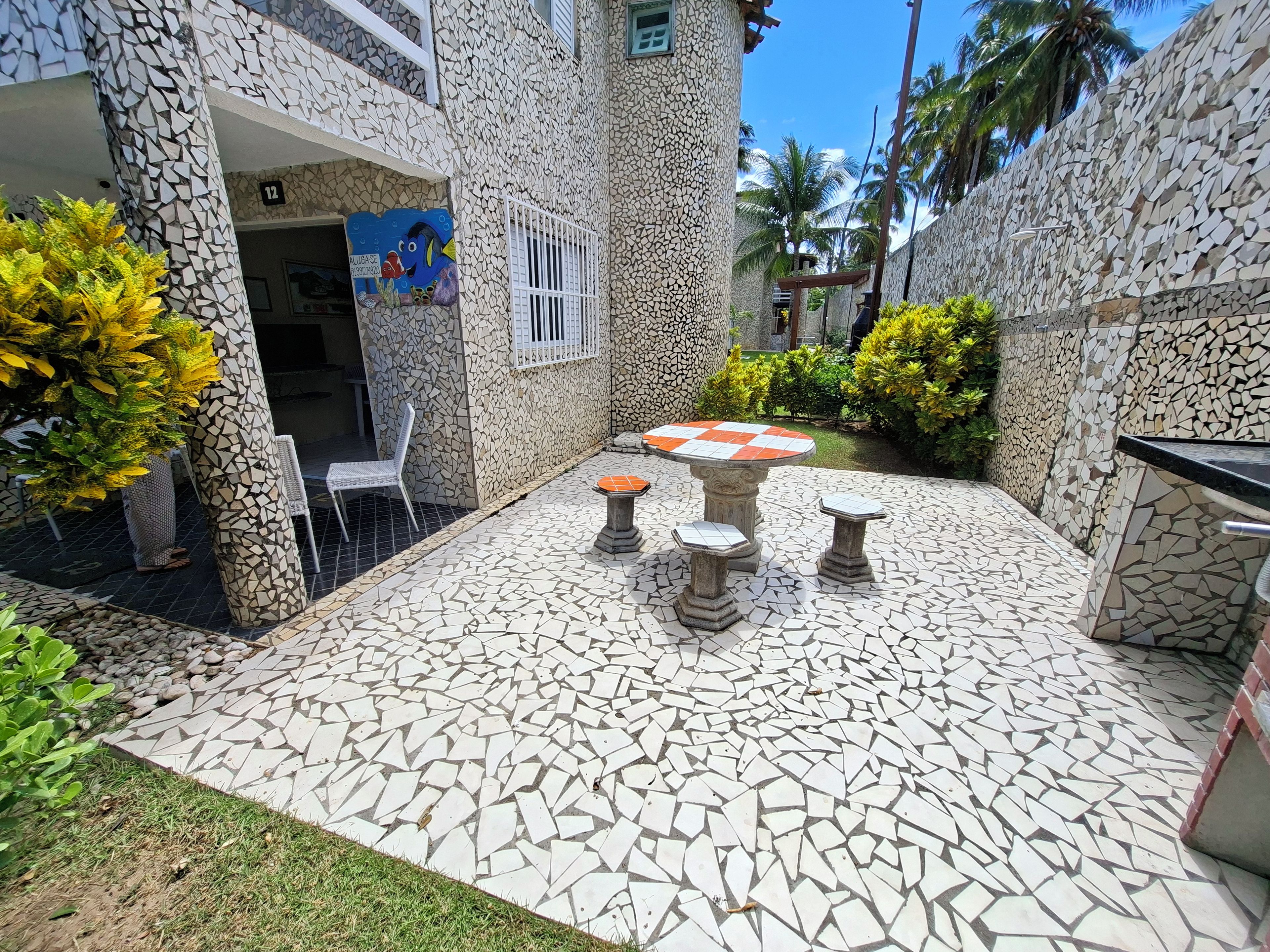 A courtyard with a mosaic-tiled floor, a round table with stools, and a chair.
