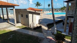 A pool area with a stone wall, palm trees, and a view of the ocean. - Chalés Village Gales (Maragogi)