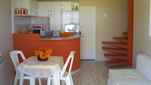 A compact kitchen with white cabinets, a dining table with chairs, and a small island with a vase of flowers. - Chalés Village Gales (Maragogi)