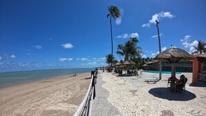 A beachside resort with a paved walkway, palm trees, and a pool area. - Chalés Village Gales (Maragogi)