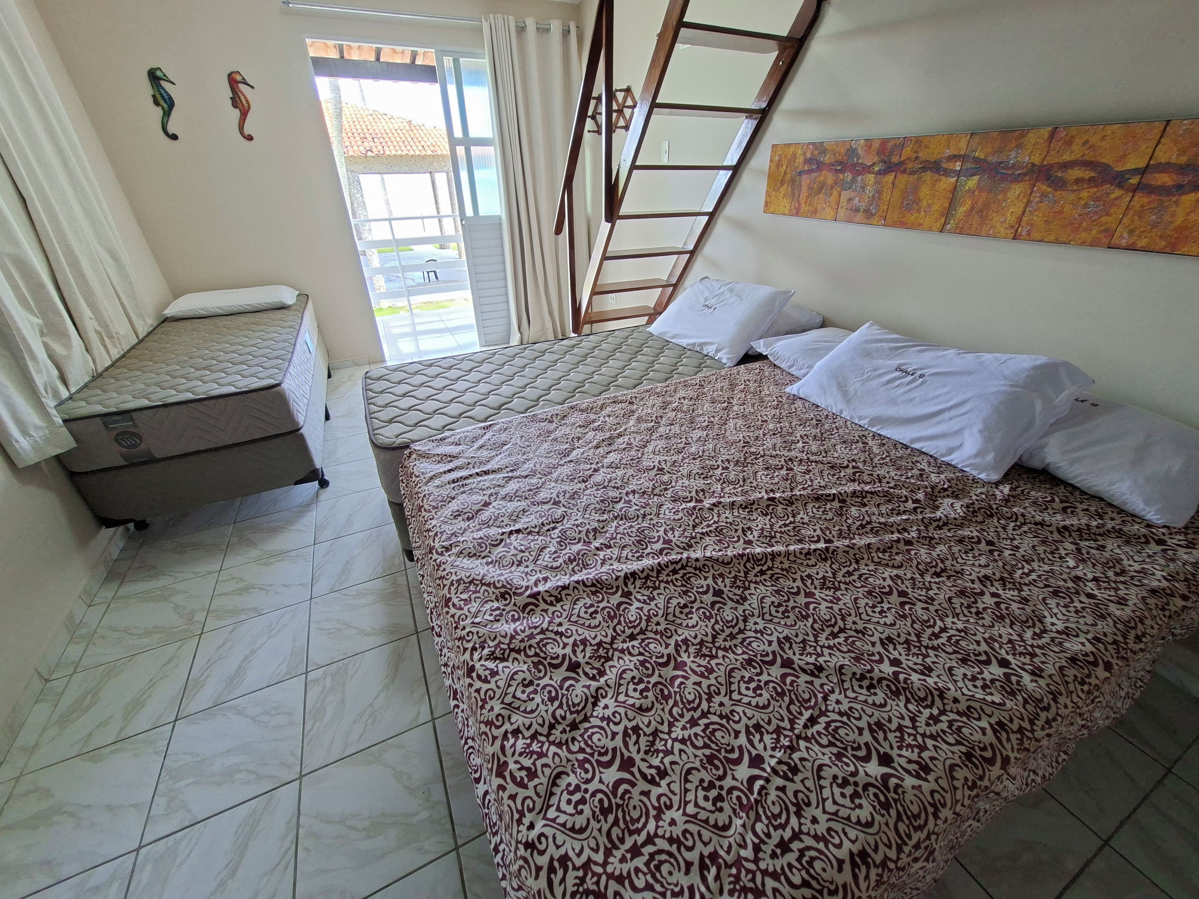 A bedroom with two beds, a window with curtains, a ladder, and a wall with a painting.