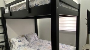 Een stapelbed met een sprei met stermotief, een raam met zonwering en een prullenbak.