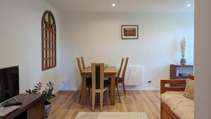Una sala de estar con una mesa de comedor de madera, sillas, un televisor, un radiador, un cuadro en la pared y un sofá.