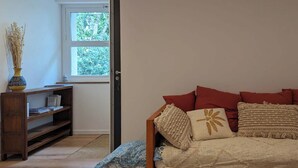 Una habitación acogedora con una cama de madera, almohadas rojas y un ventanal con vistas al verdor.