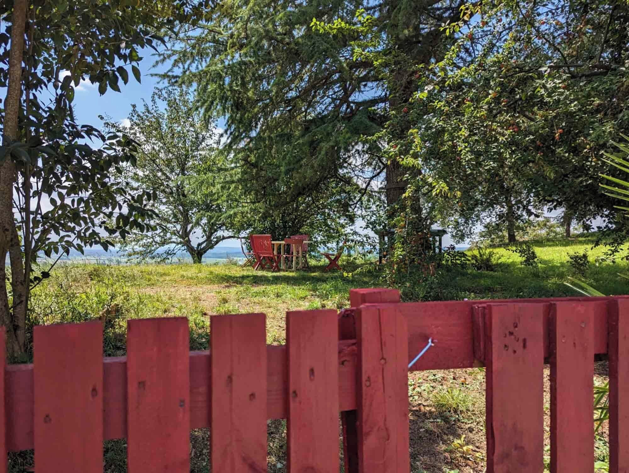 A red wooden fence in a lush green landscape with trees and a clear sky.
