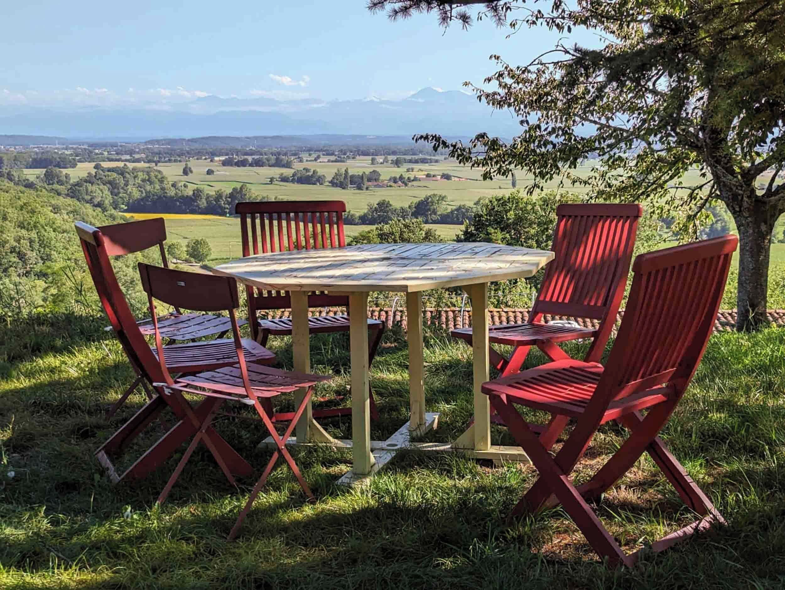 Una mesa y cuatro sillas colocadas al aire libre, con una vista panorámica de un valle y montañas al fondo.