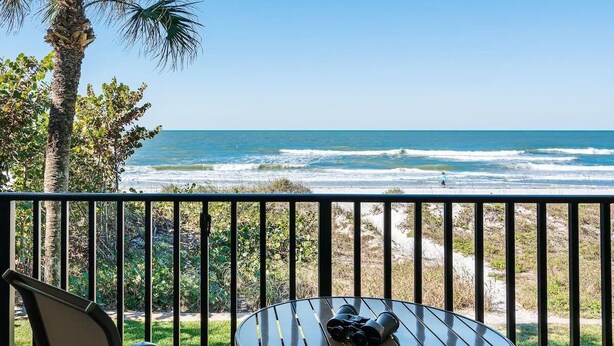 A balcony with a table and chairs overlooking the ocean.