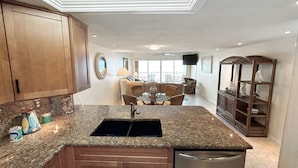 A kitchen with granite countertops, wooden cabinets, a stainless steel dishwasher, and a dining area with a round table and chairs.