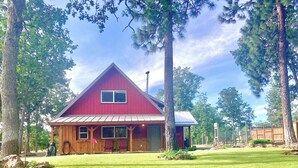 A red wooden cabin with a gabled roof, a porch, and a fenced yard. - Abundant Activities for Adventures People (Goldendale)