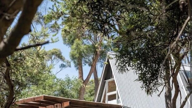 Une maison unique, dotée d’un toit en pente et d’une pergola en bois avec des chaises.