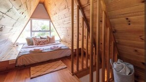 Une chambre mansardée chaleureuse avec un plafond en pente, des murs en bois, un lit avec des oreillers et une fenêtre.