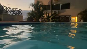 Une piscine à l’eau claire, entourée de palmiers et bordée d’un bâtiment aux grandes fenêtres.