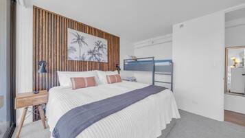 Une chambre avec un lit superposé, un mur recouvert de panneaux de bois, un grand lit avec une literie blanche, une table de chevet avec une lampe et un miroir sur le mur.