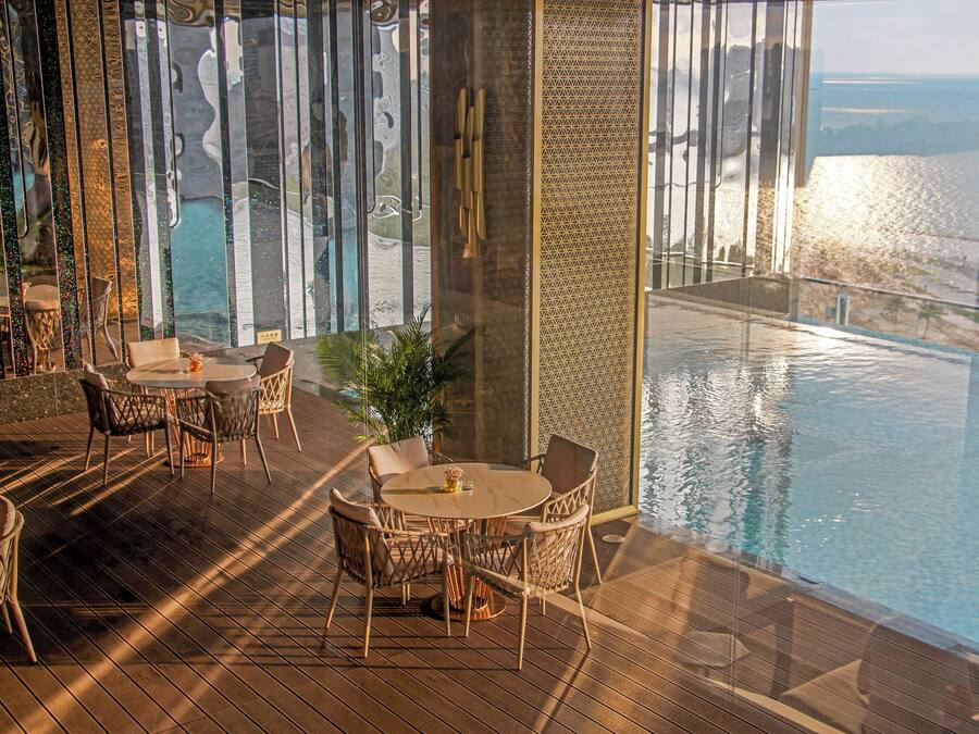 Ein Poolbereich mit Tisch und Stühlen, Blick auf den Ozean und einer Glasbarriere.