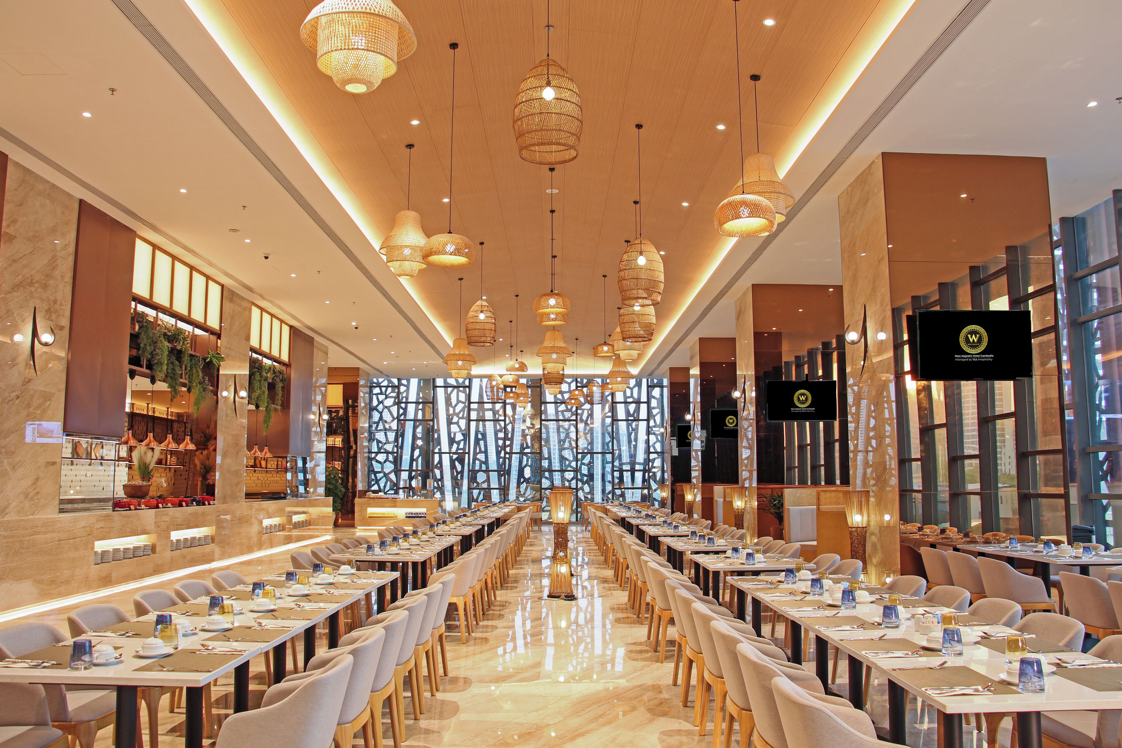 A spacious conference room with long tables, modern chandeliers, and a large screen at the front.