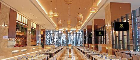 A spacious conference room with long tables, modern chandeliers, and a large screen at the front.