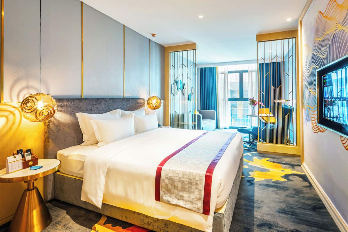A hotel room with a large bed, bedside tables, a TV, and a view of the outside.