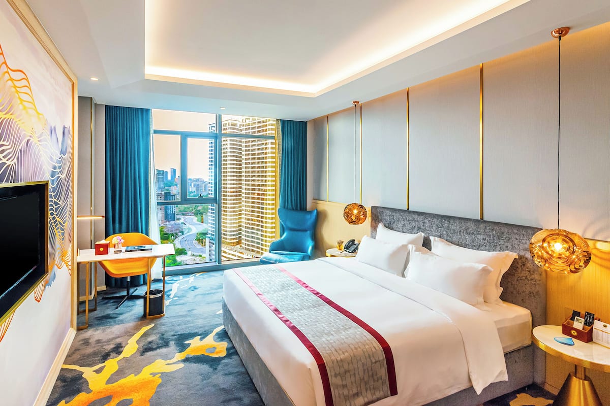 A hotel room with a large bed, a desk with a chair, a TV, and a view of the cityscape.