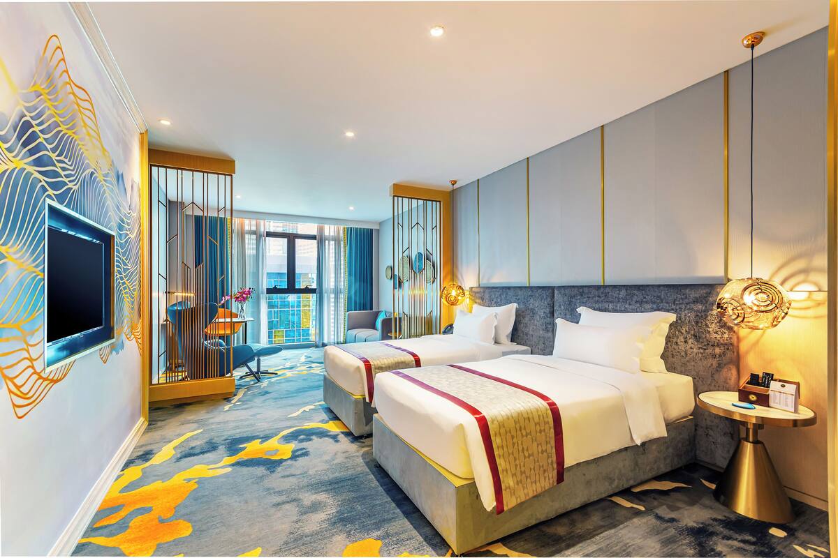 A hotel room with two beds, a TV, a bedside table, and a view of the city.