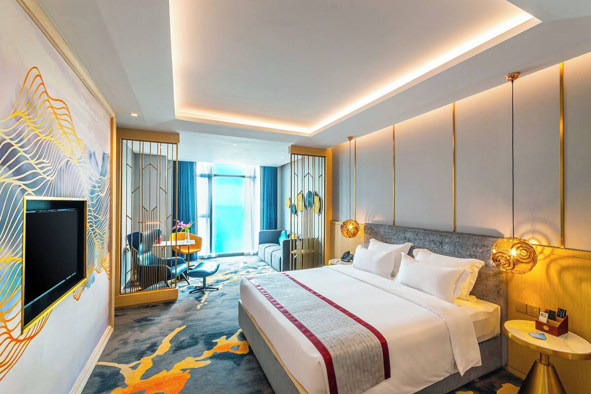 A modern hotel room with a large bed, a TV mounted on the wall, a desk, and a view of the outdoors.