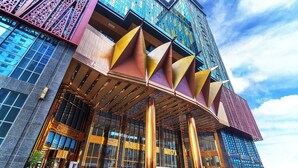 A modern building with large glass windows, a prominent entrance with a metal canopy, and a sky with clouds. - Won Majestic Hotel Cambodia (Sihanoukville)