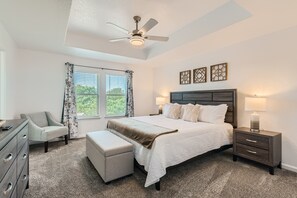 Relax in a spacious bedroom with a large bed, nightstand, chair, and dresser, offering a peaceful view of the surrounding greenery.