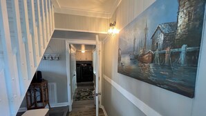 A hallway with a painting of boats on water, a staircase, and a door leading to a kitchen area. - Deep-Water Canal Front Coastal Cottage Only Steps to the Beach & Pet Friendly!  (Surf City)