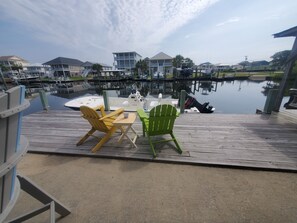 A wooden dock with two Adirondack chairs and a table, overlooking a marina with boats and houses in the background. - Deep-Water Canal Front Coastal Cottage Only Steps to the Beach & Pet Friendly!  (Surf City)