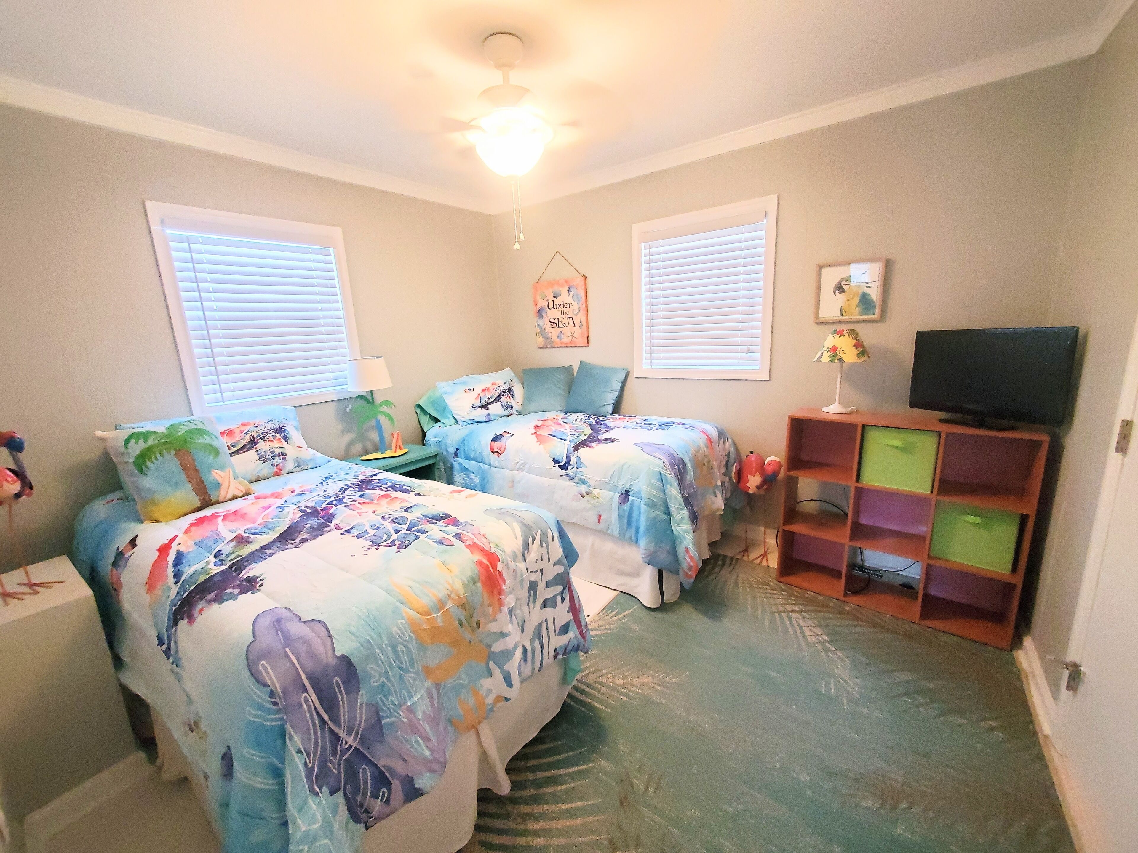 A bedroom with two beds, a ceiling fan, a TV, and a bookshelf.