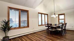 A spacious dining area with a high ceiling and large windows, wooden flooring, and a central table with chairs. - Newly Renovated 4BR 2BA Ocean Block Bay View Ship Bottom Home Central Location  (Ship Bottom)